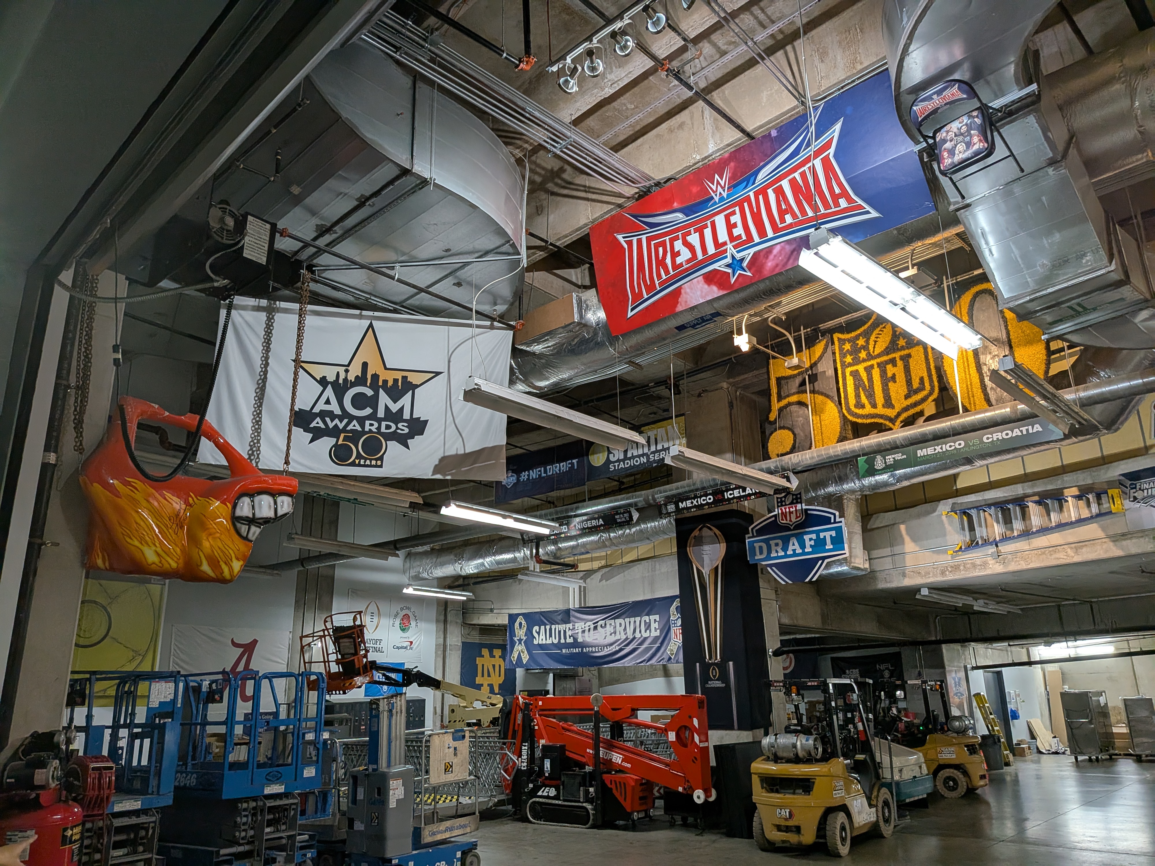 A photograph of a storage area with memorabilia including banners for WresleMania, the ACM Awards, and the NFL Draft